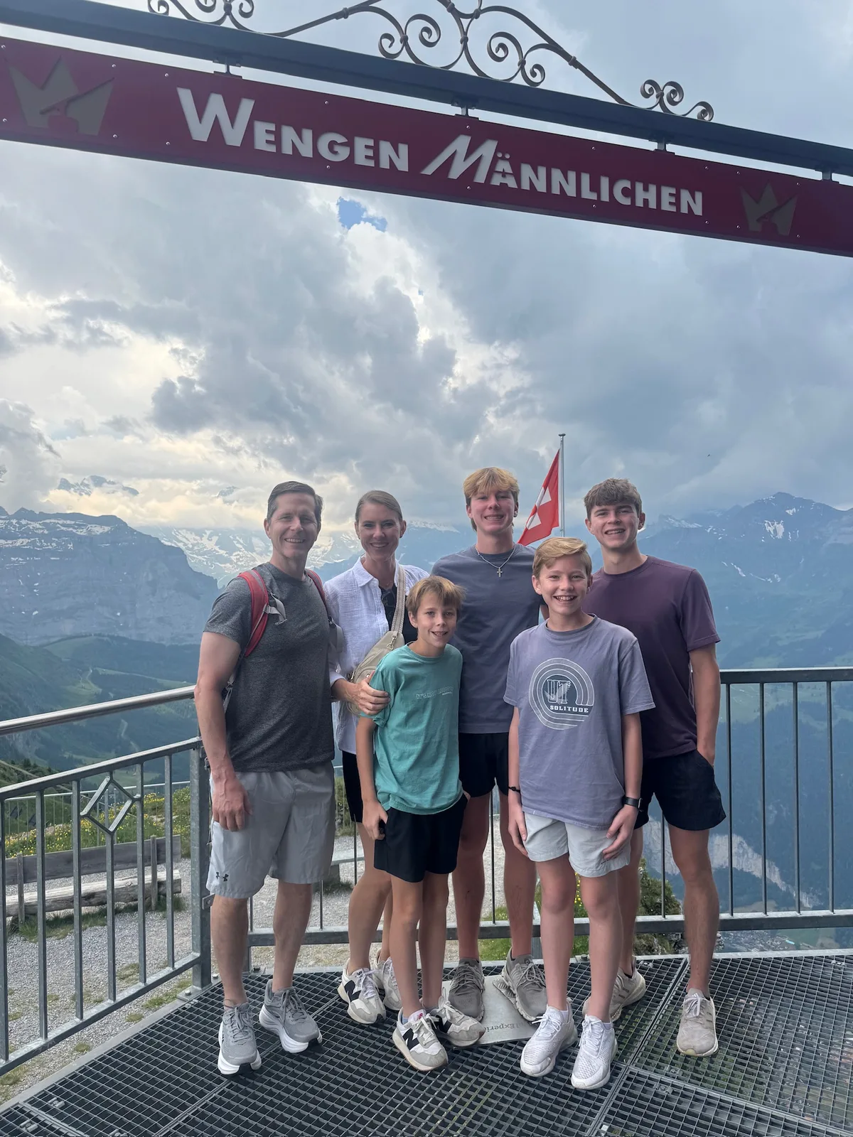 Family together beneath the Wengen–Männlichen sign with mountains behind them