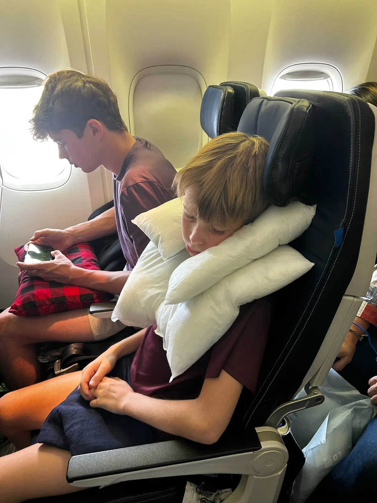 Children resting in airplane seats with travel pillows