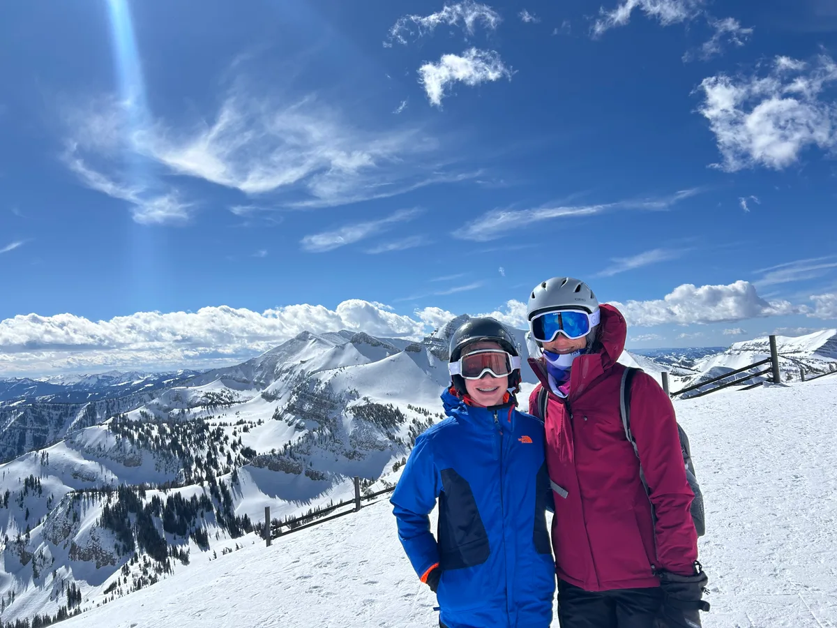 Angela and one of the boys in ski gear above a snowy mountain panorama